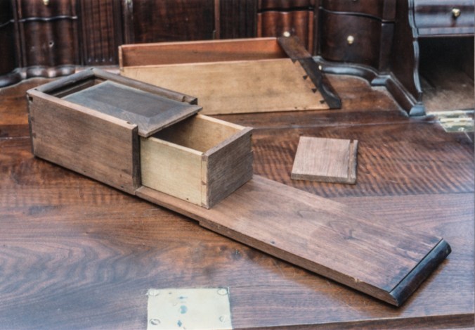 When the lower drawers at the sides of the interior are pulled out, a spring lock, accessed from the upper long drawer of the case, is sprung to allow a section of the ledge under the drawers to be pulled out reveling a hidden drawer.