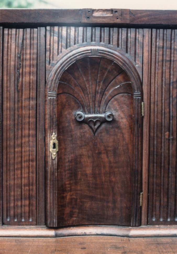 The prospect door is dished with a carved fan and a heart motif. Like the drawers it is made from figured black walnut.